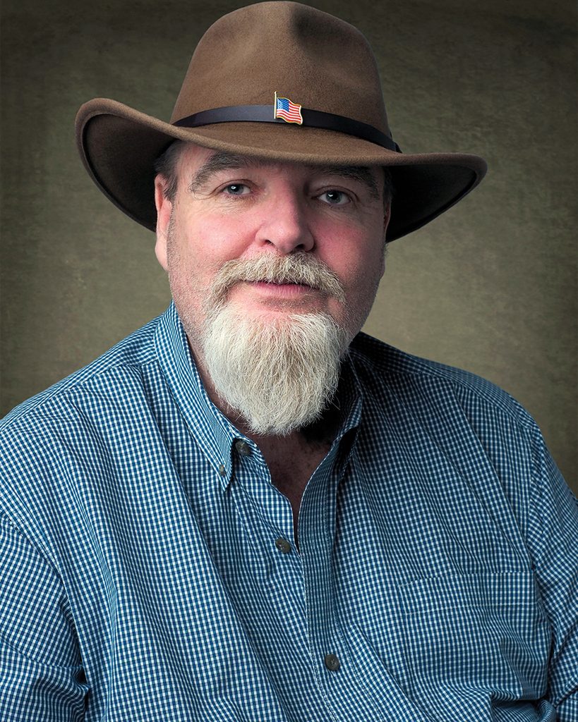 Portrait of M. Kameron Hawkins wearing a cowboy hat and blue checkered shirt.